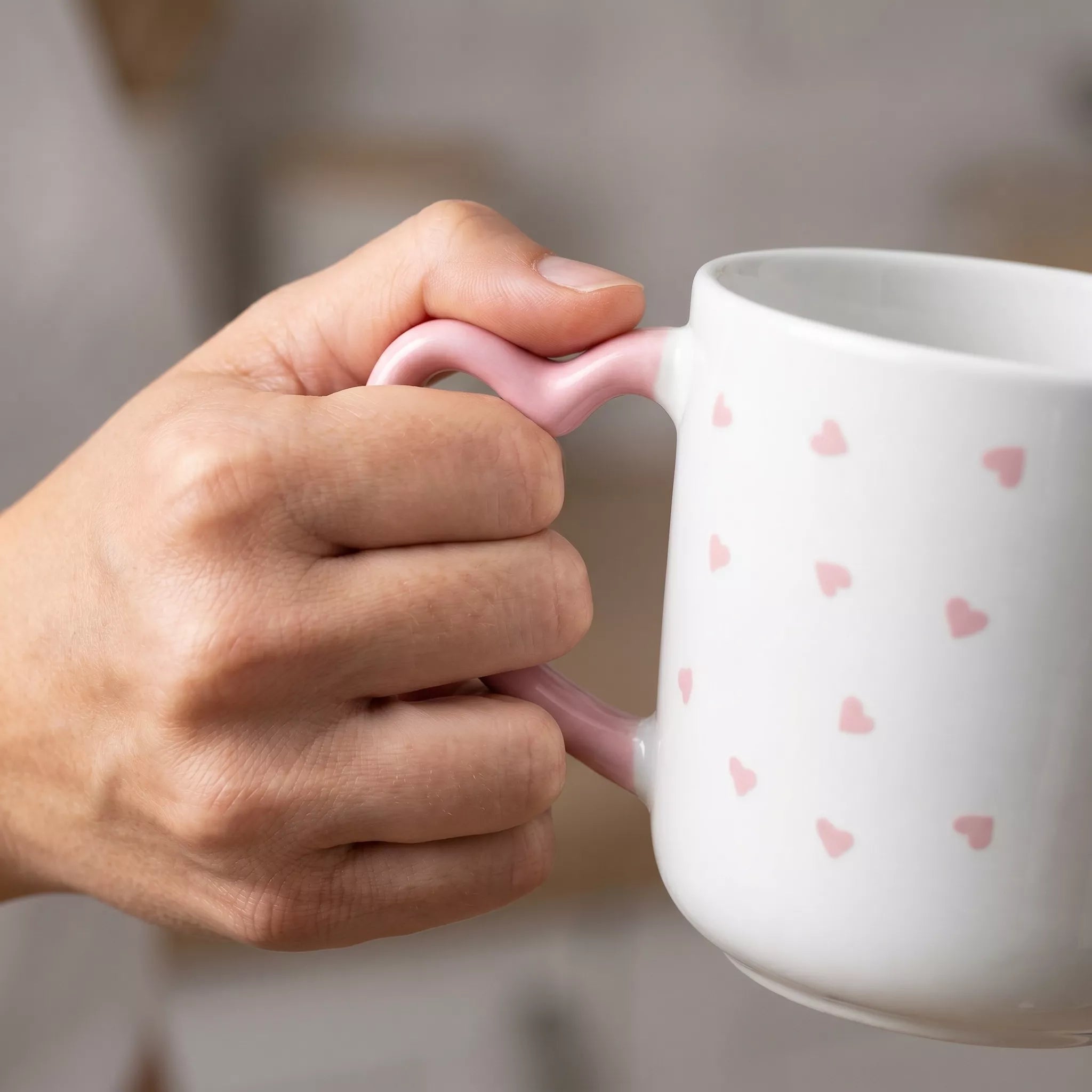 Hand holding a white mug with pink heart patterns