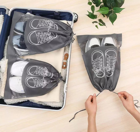 Gray shoe bag travel organizers shown being packed into a suitcase and held open by hands, with white sneakers visible inside and printed shoe illustrations on the bags.