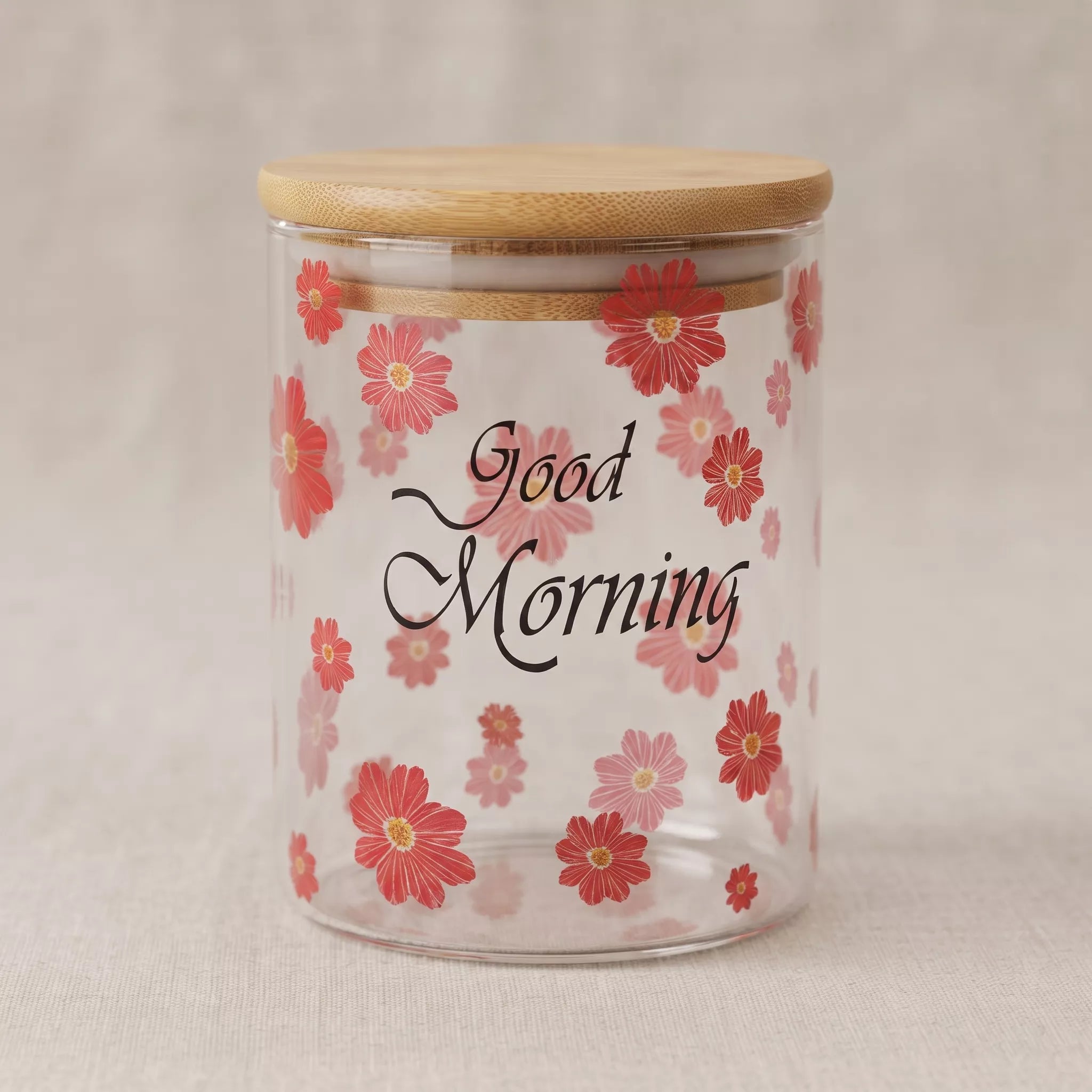 A clear glass jar with a light wood bamboo lid, decorated with red and pink flowers and the words 'Good Morning' in black script.
