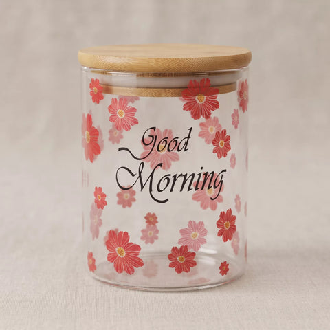 A clear glass jar with a light wood bamboo lid, decorated with red and pink flowers and the words 'Good Morning' in black script.