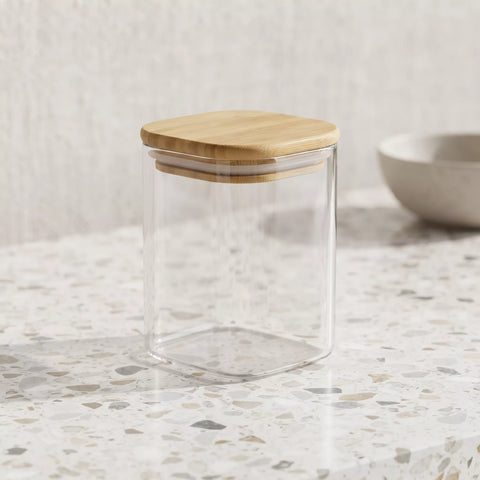 Clear glass canister with a square bamboo lid, shown on a speckled countertop with a neutral background.