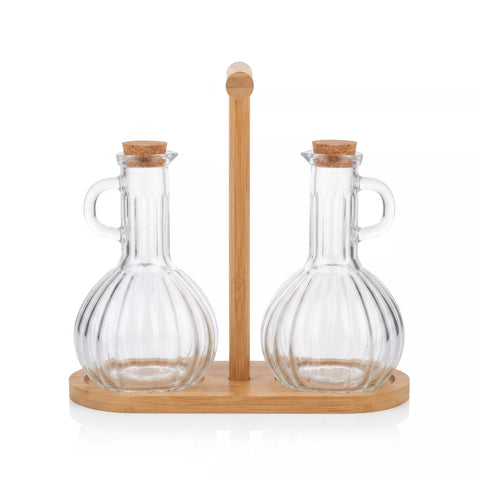 Two clear ribbed glass oil or vinegar bottles with cork stoppers and small handles, displayed on a light wood stand with a vertical handle.