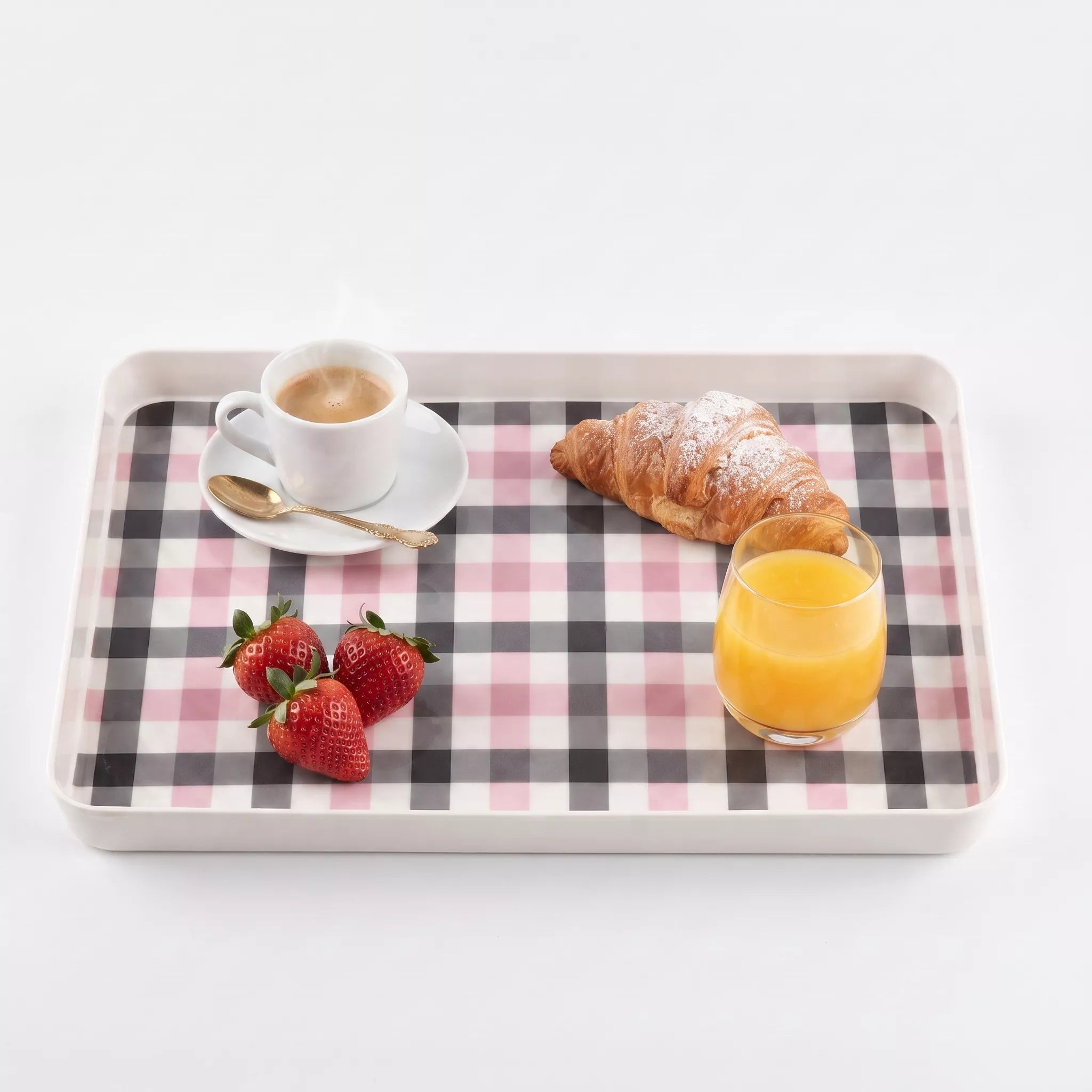 A rectangular serving tray with a pink, black, and white gingham check pattern, styled with a cup of coffee, a croissant, strawberries, and a glass of orange juice on a white background.