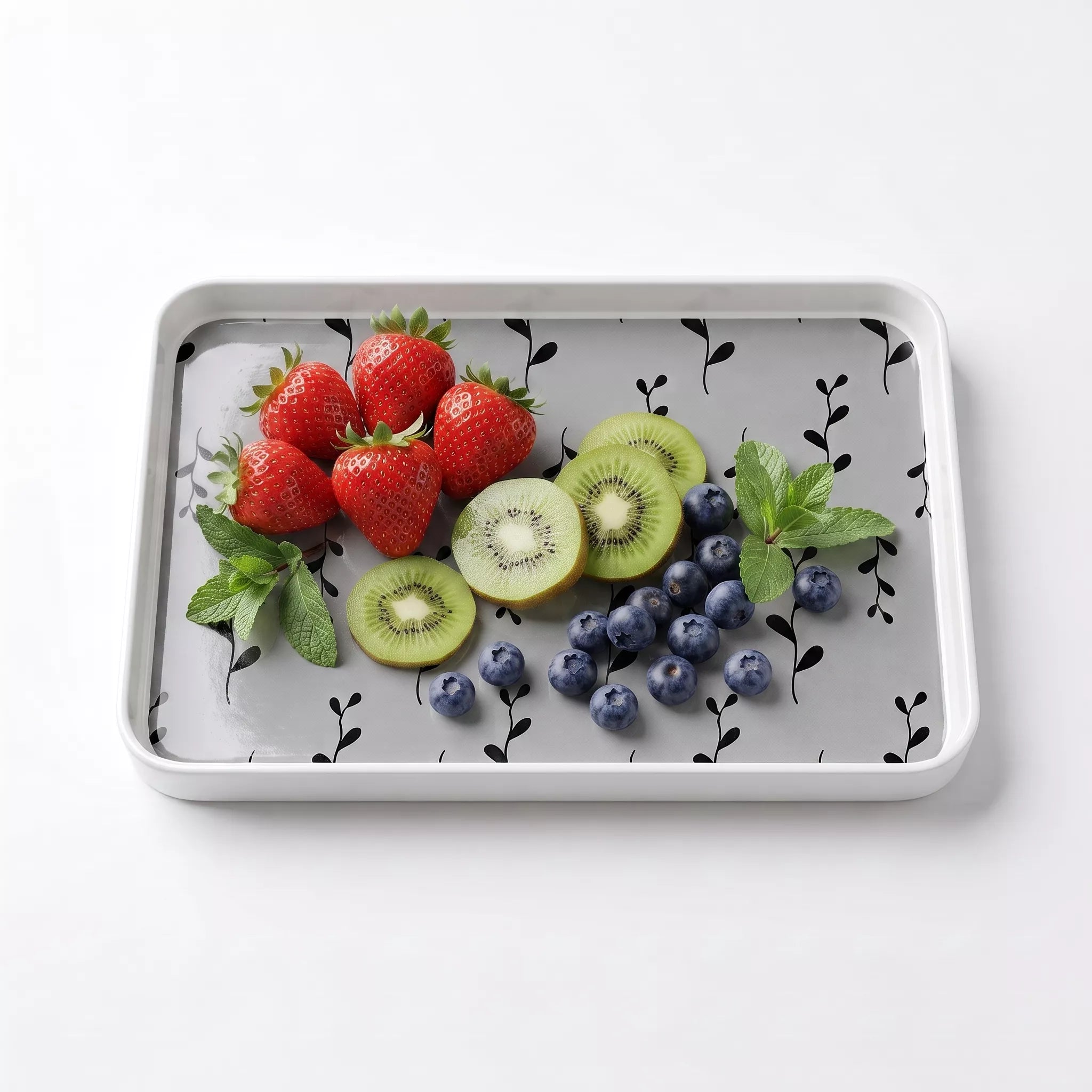 A rectangular gray tray with a black leaf pattern, shown from a top-down view on a white background. The tray is styled with fresh fruit, including strawberries, sliced kiwi, blueberries, and mint leaves.